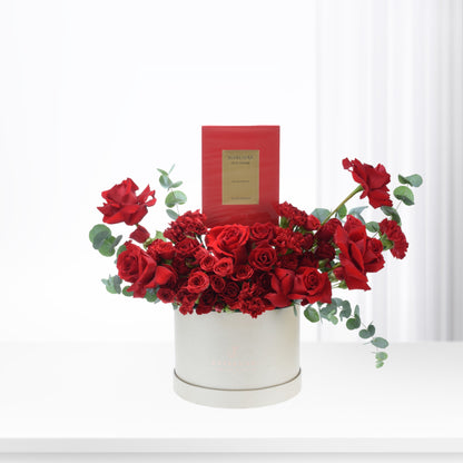 Vibrant red roses and carnations in cream box, accented with eucalyptus and luxury perfume.