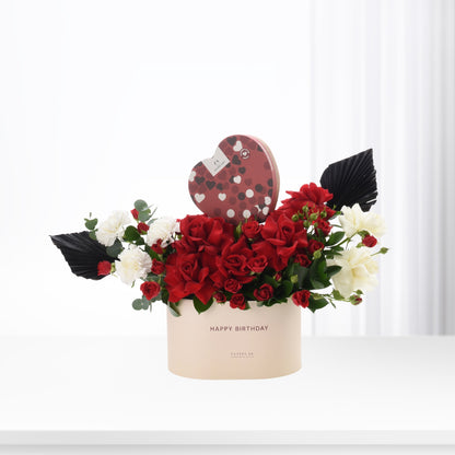 Elegant birthday bouquet with red roses, white blooms, and heart-shaped chocolate box.