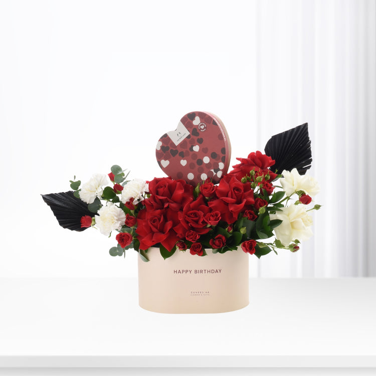 Elegant birthday bouquet with red roses, white blooms, and heart-shaped chocolate box.