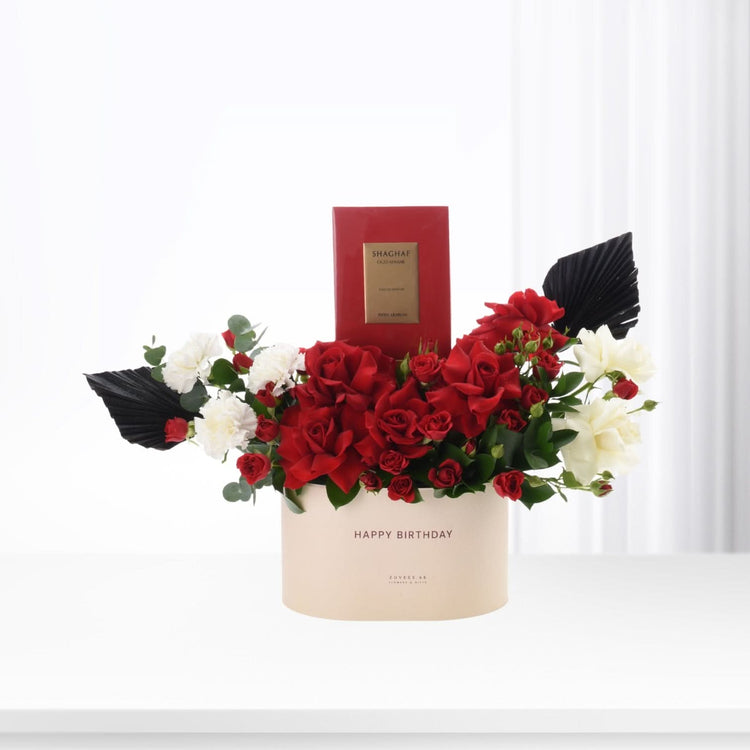 Elegant red roses and white blooms in beige box with "Happy Birthday" and luxury perfume.