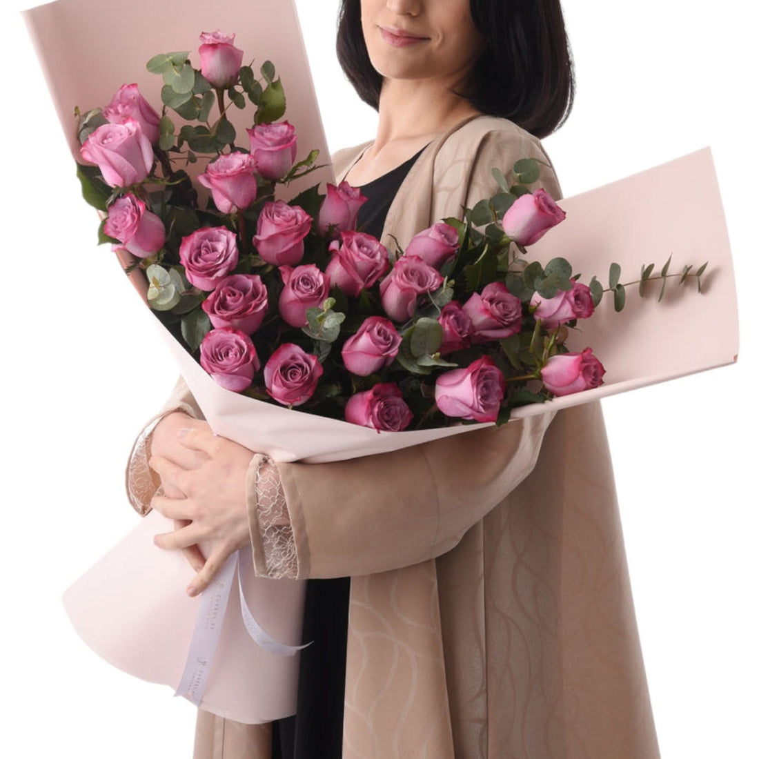Soft pink roses wrapped in blush paper, held by a smiling woman.
