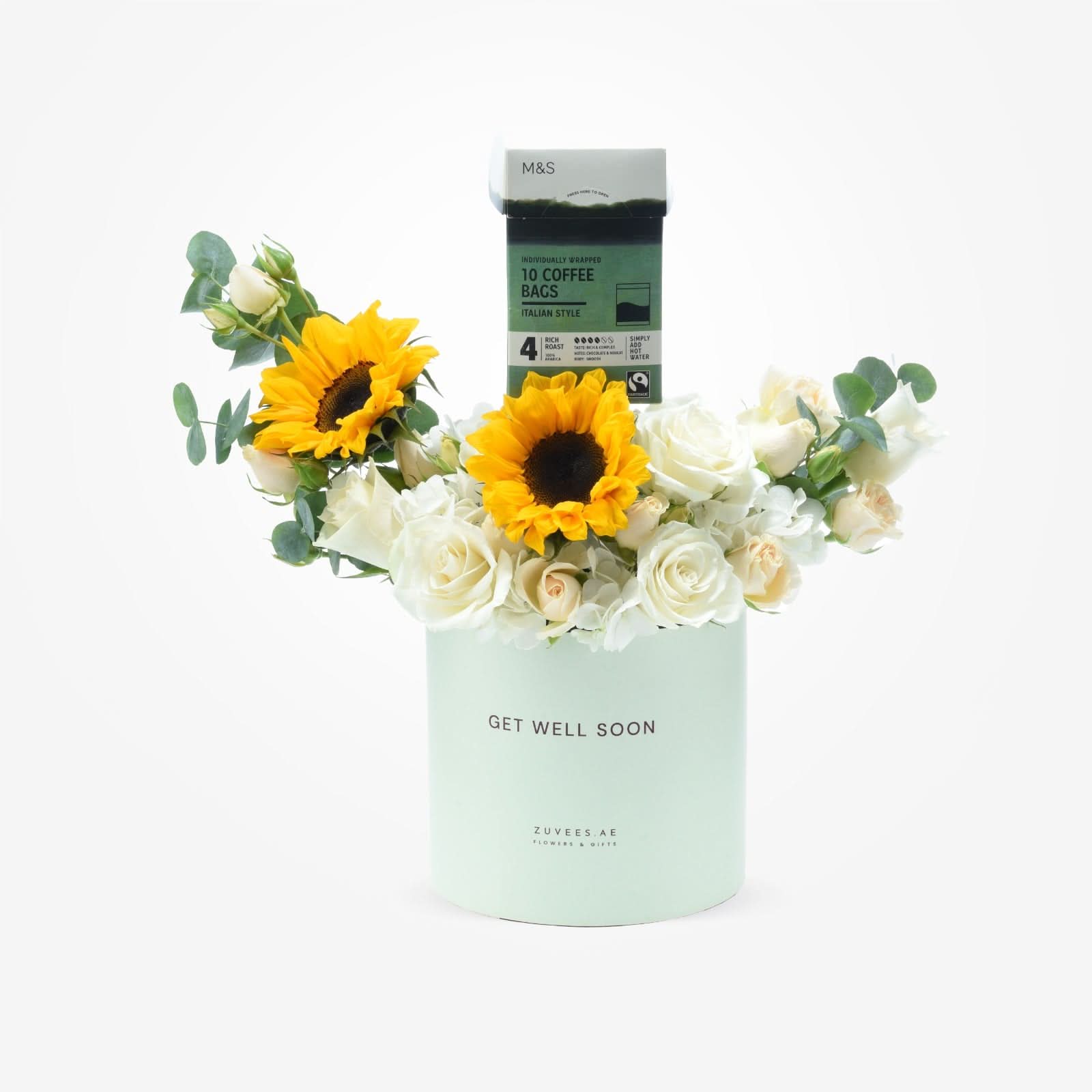 Pastel mint cylinder holds white roses and sunflowers, topped with M&amp;S coffee, "Get Well Soon" message.