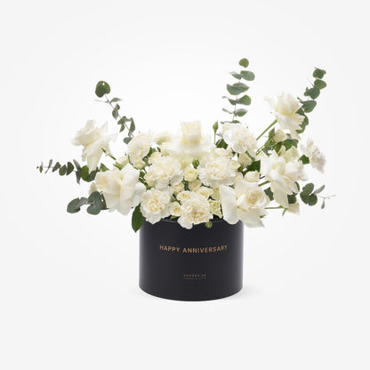 Elegant white roses and eucalyptus in black box with gold "Happy Anniversary" text.