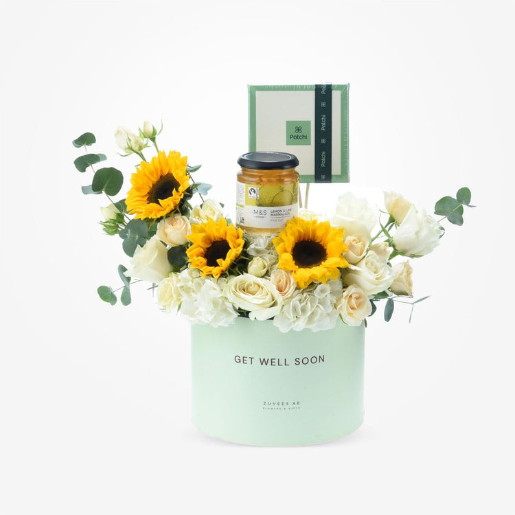 Pastel green box holds vibrant sunflowers, white roses, and marmalade for get-well-soon gift.