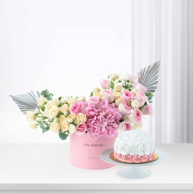 Pink floral arrangement with silver accents beside a pink-and-white cake.