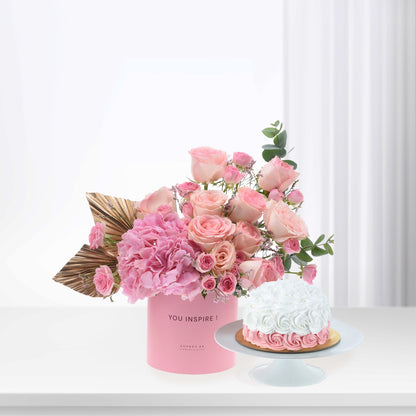 Pink roses and hydrangeas in branded box beside white rose cake.