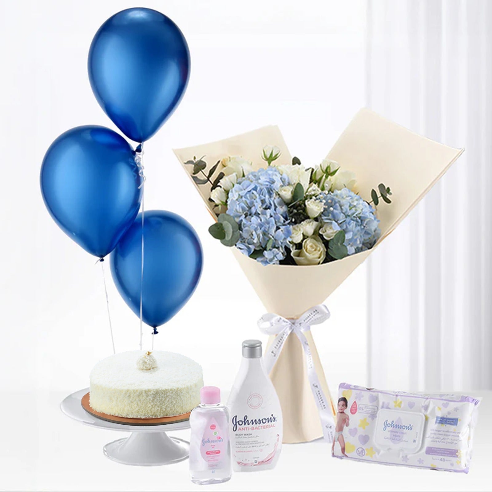 Blue balloons, hydrangea bouquet, cake, and Johnson’s baby care products arranged elegantly.