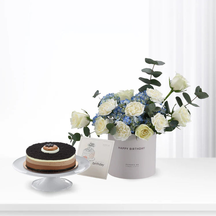 Elegant birthday gift set: chocolate cake, white roses, blue hydrangeas, and "Happy Birthday" card.