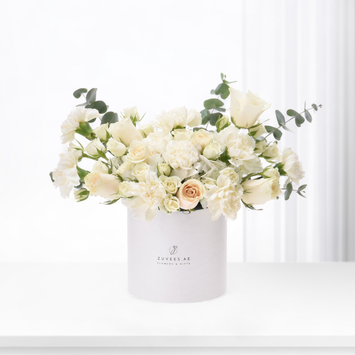 Elegant white rose and carnation bouquet in branded white cylindrical vase.