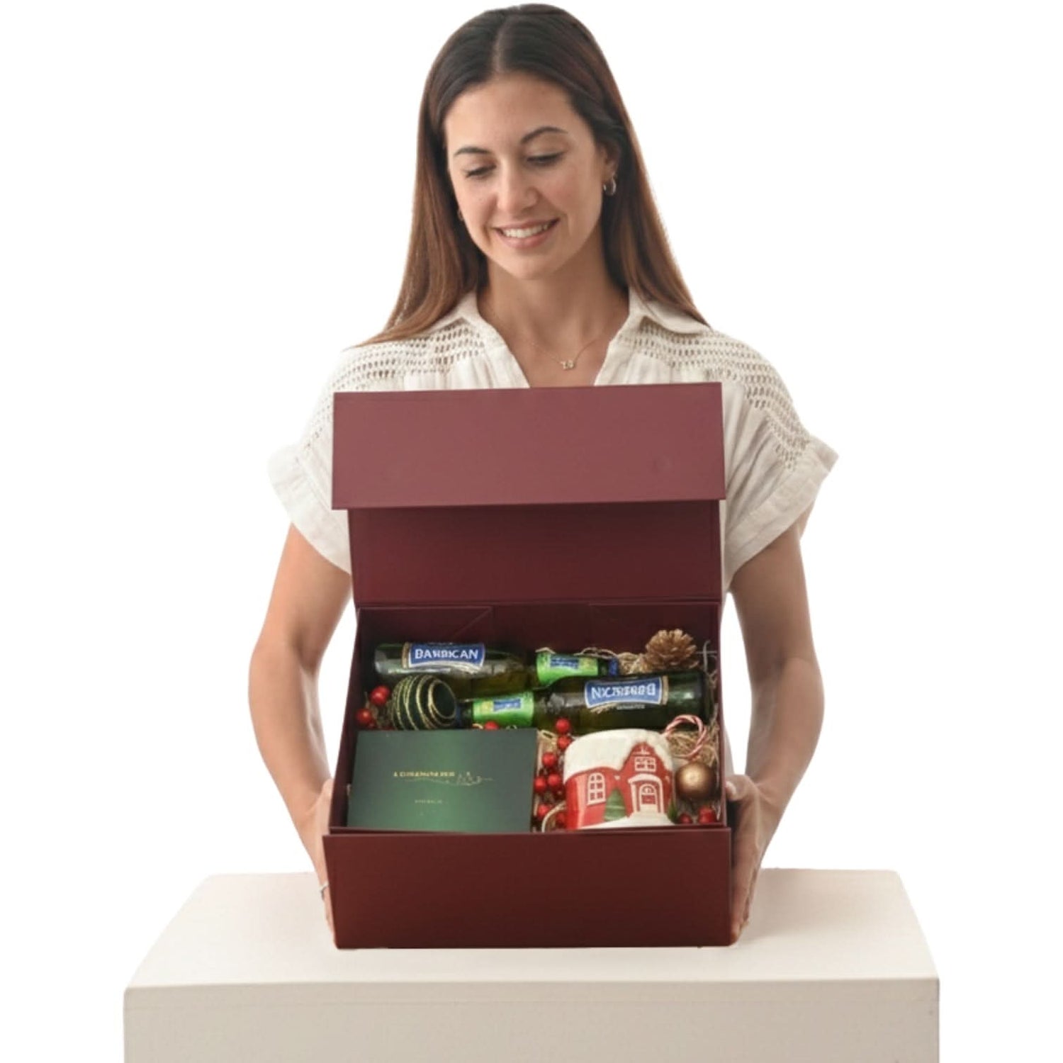 Woman holds festive red gift box with wine, ornaments, and holiday mug inside.