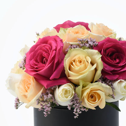 Vibrant pink, peach, and cream roses with purple filler in sleek black cylinder vase.