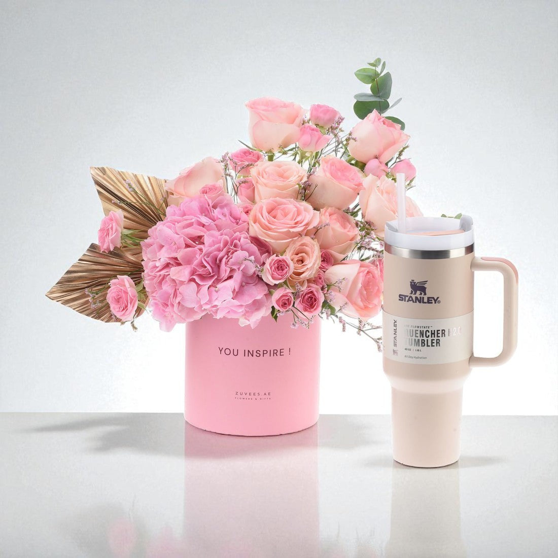 Pink floral arrangement beside matte beige Stanley tumbler with straw.