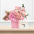 Pink roses and hydrangeas in a "You Inspire!" cylinder, beside matching card on wood.