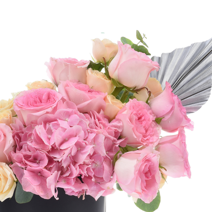 Pink roses, hydrangeas, silver wrap, dew-kissed petals, lush bouquet in black vase.