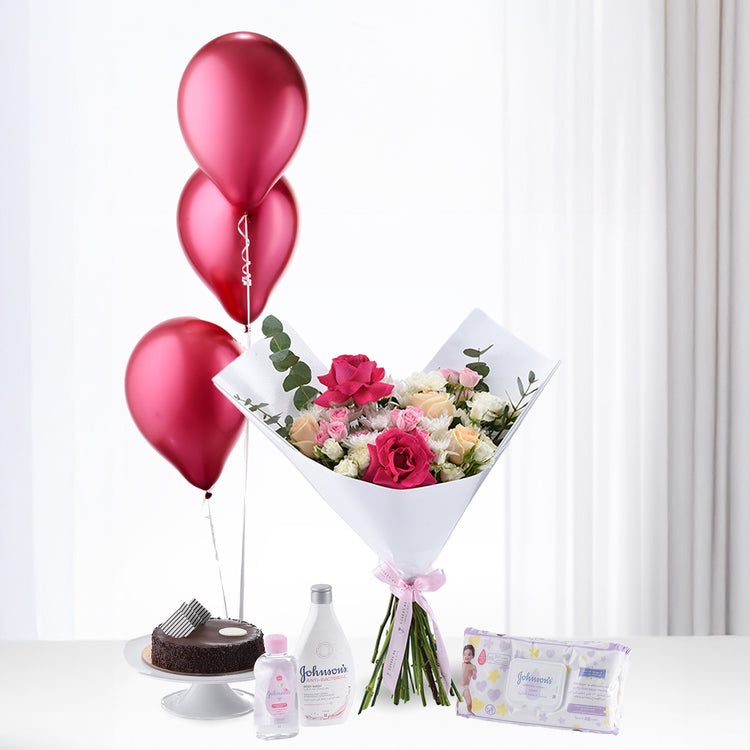 Shimmering red balloons rise beside floral bouquet, baby essentials, and chocolate cake.