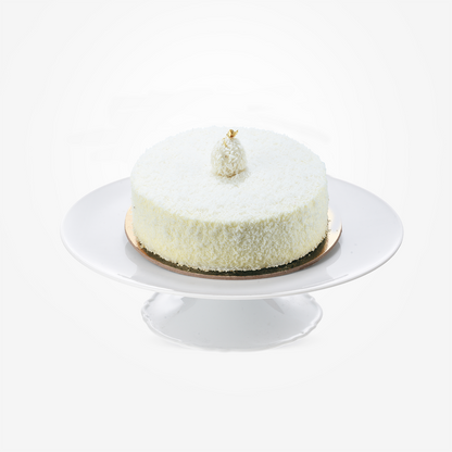 White coconut cake topped with gold leaf, elegantly displayed on a white cake stand.