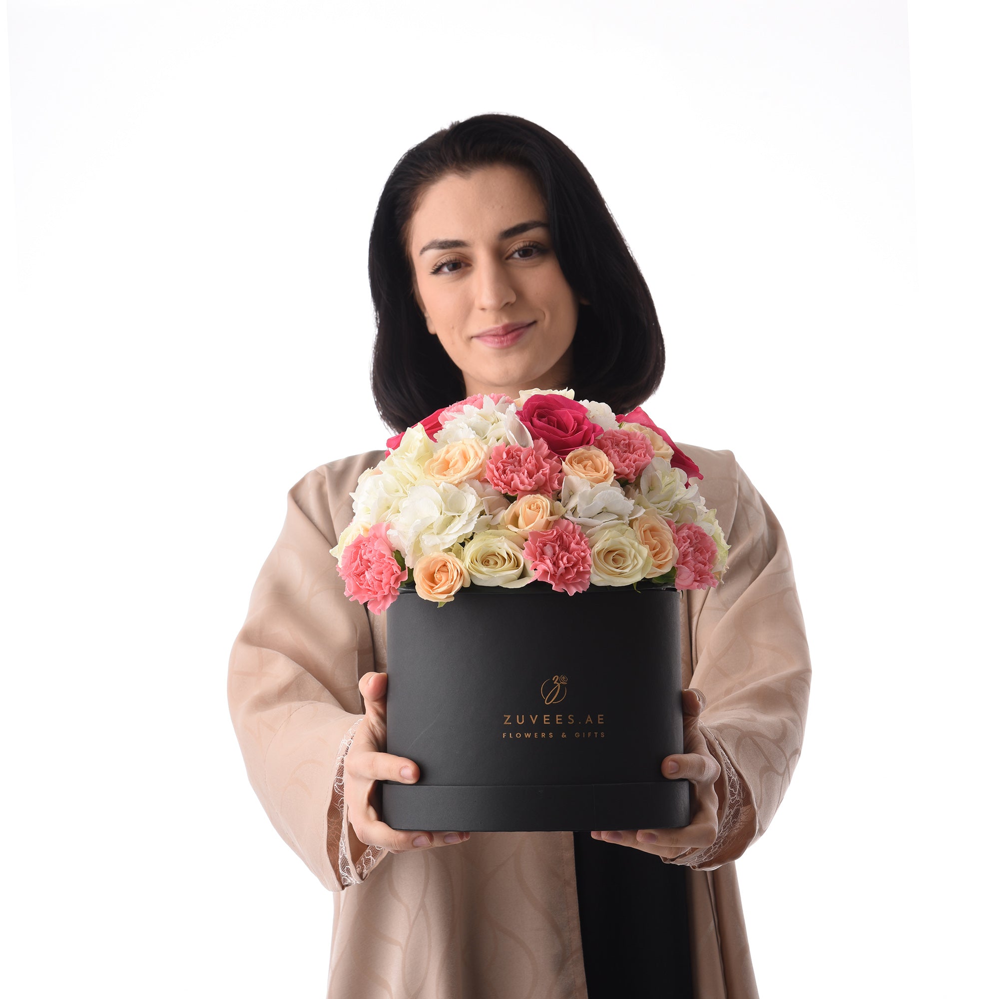 Elegant woman holds luxurious black box overflowing with vibrant pink, peach, and white roses.