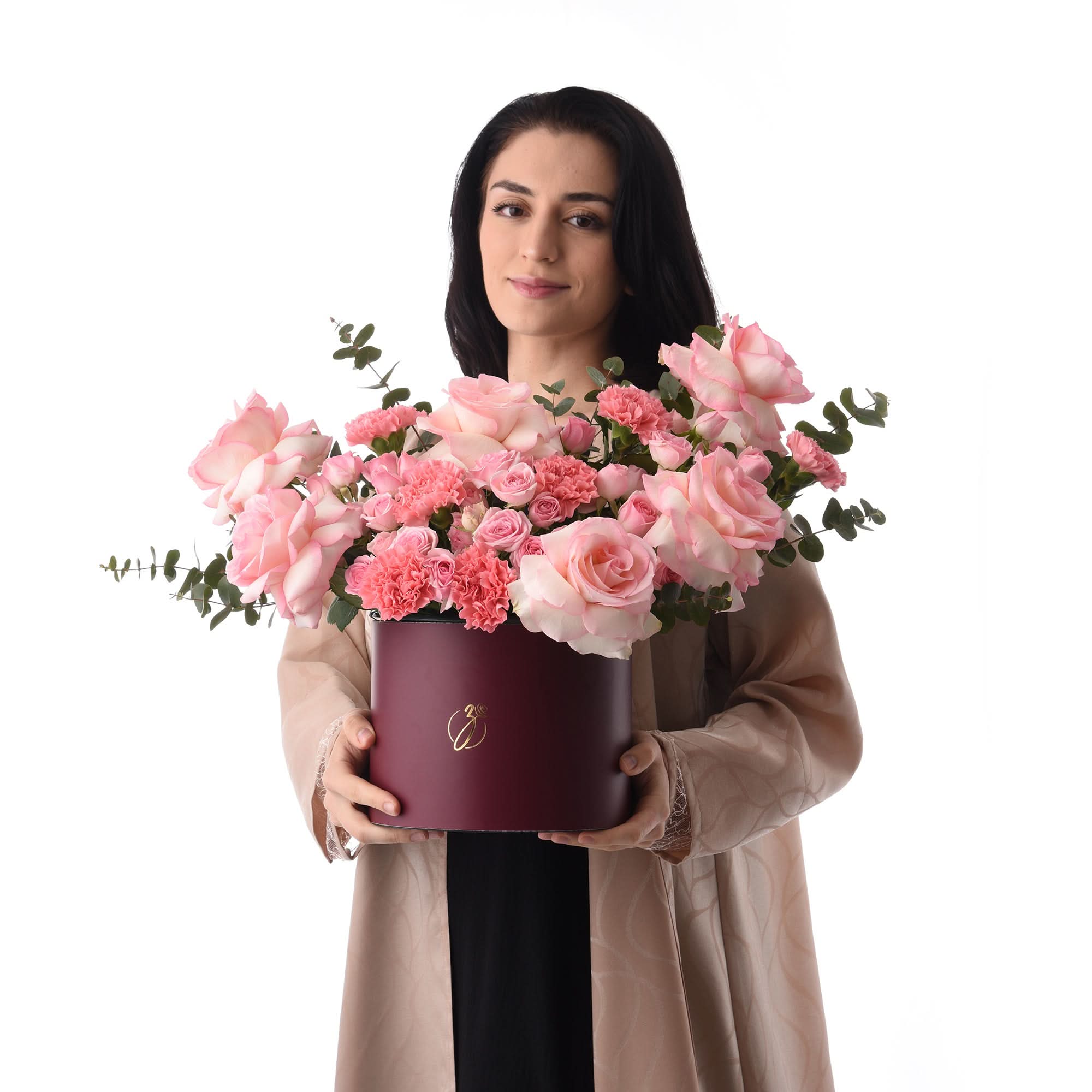 Woman holds burgundy hat box overflowing with pink roses and carnations.