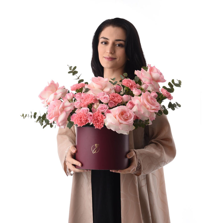 Woman holds burgundy hat box overflowing with pink roses and carnations.