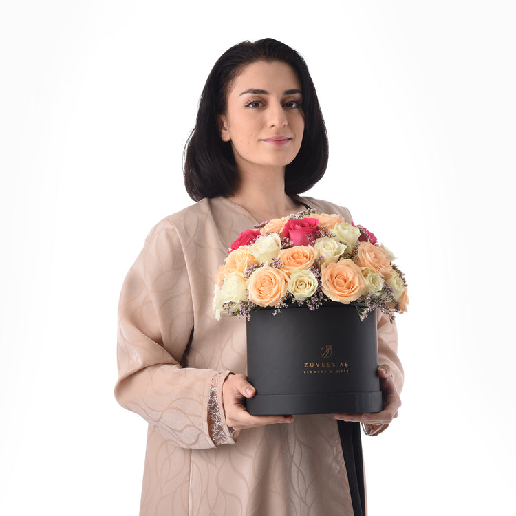 Elegant woman holds black box of vibrant multi-colored roses.