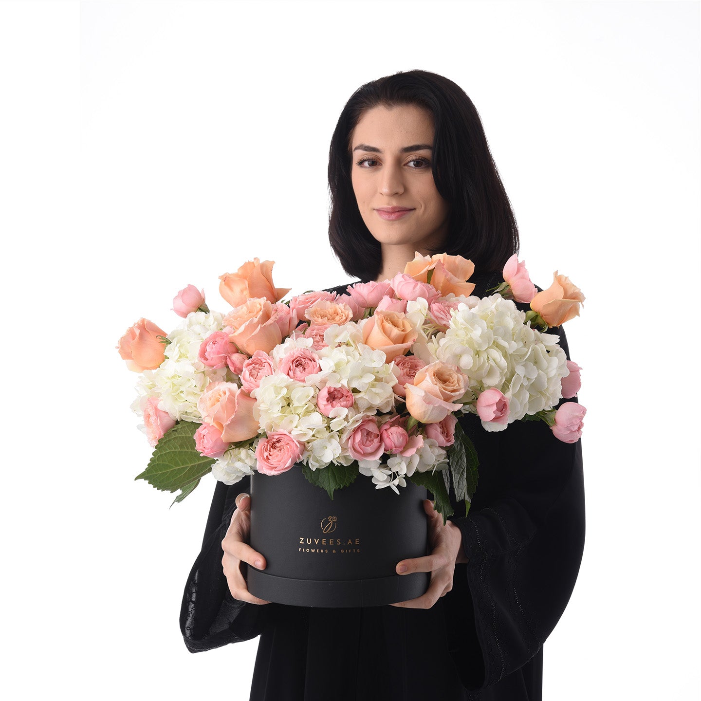 Elegant woman holds lush pink peach white rose and hydrangea bouquet in sleek black box.