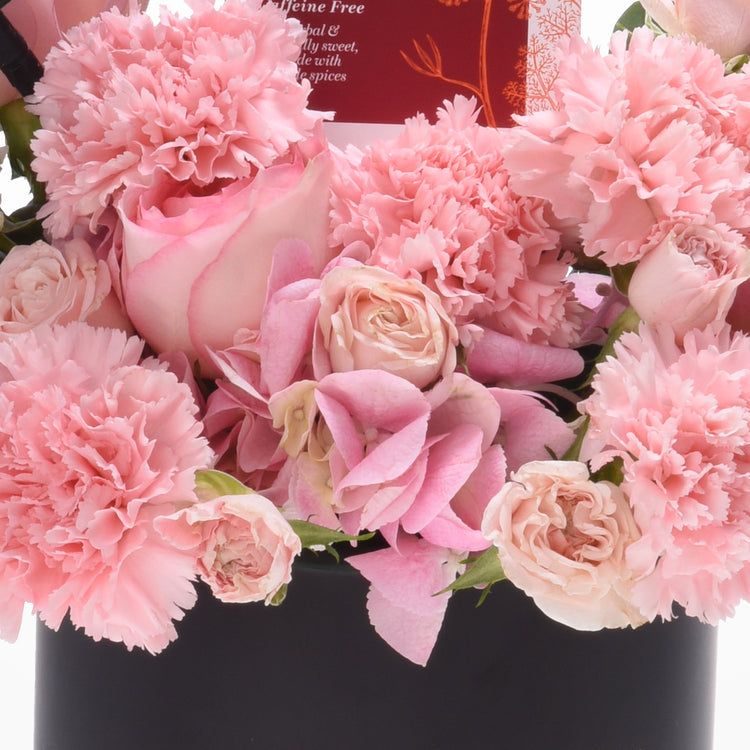 Soft pink carnations and roses bloom lushly in sleek black vase.