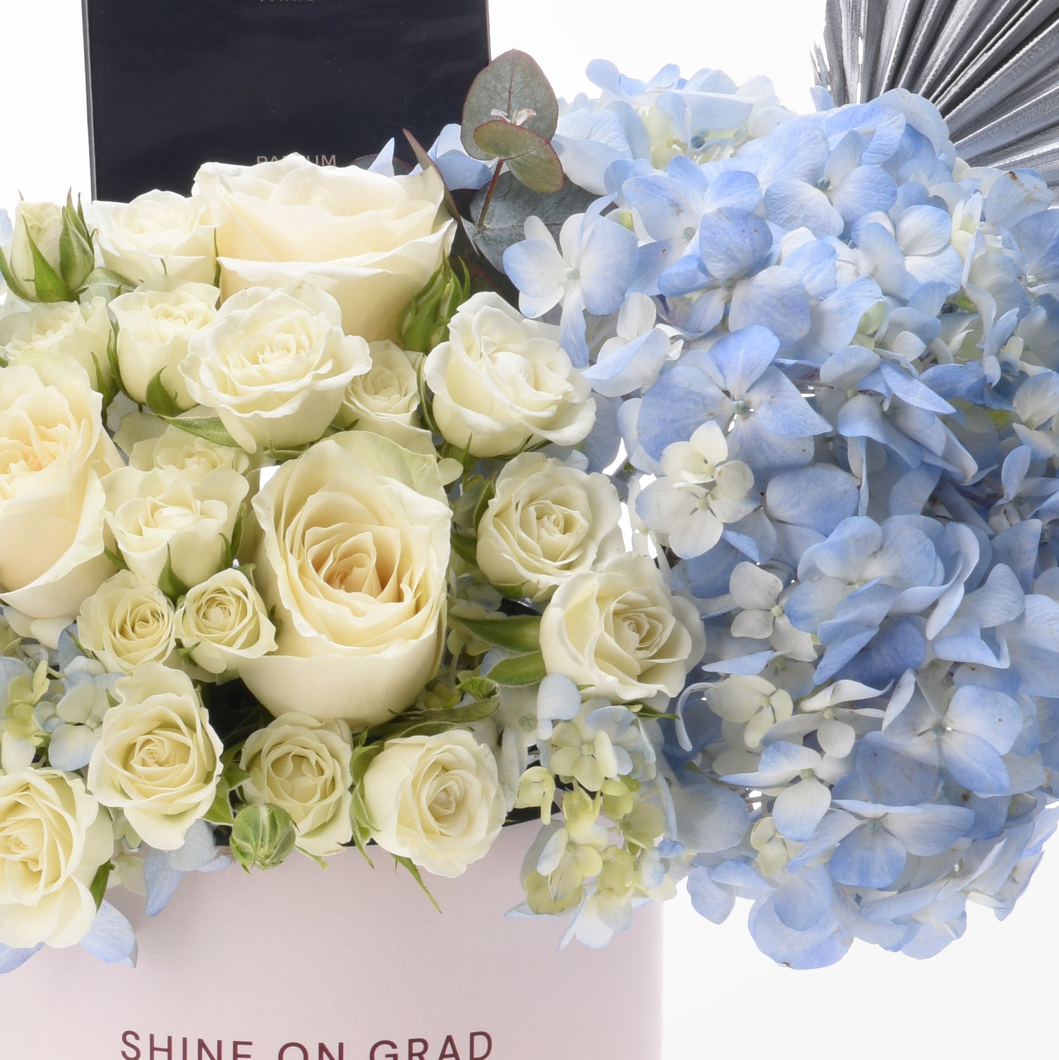 Cream roses and blue hydrangeas in elegant pink box with "Shine On Grad" text.