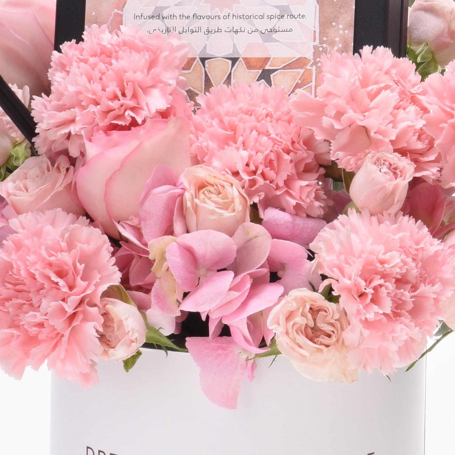 Soft pink carnations, roses, and hydrangeas bloom vibrantly in a white vase.