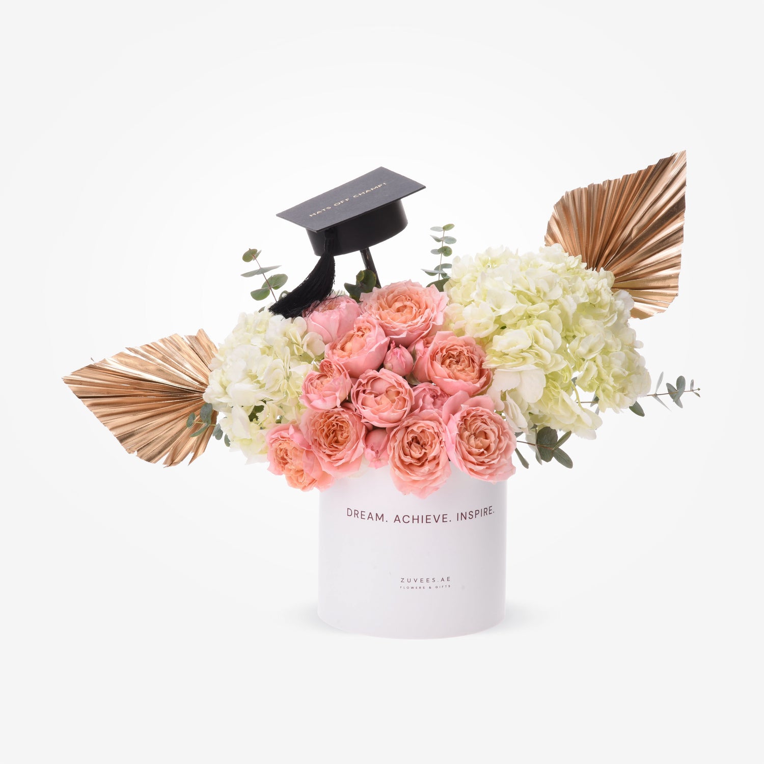 Pink roses, white hydrangeas, gold palms, and a black grad cap in a white "Dream. Achieve. Inspire." box.