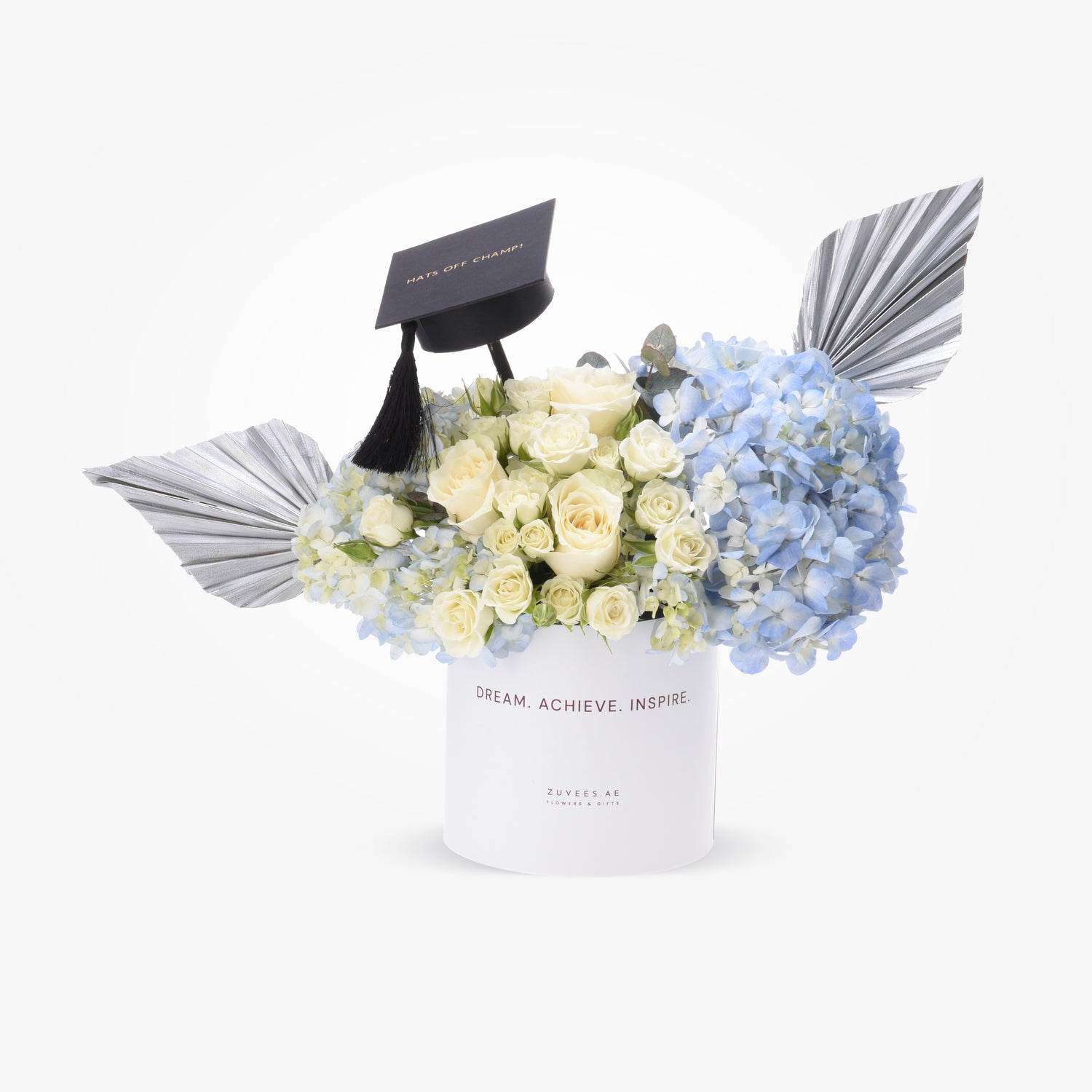 White roses and blue hydrangeas in sleek white box with graduation cap and silver wings.