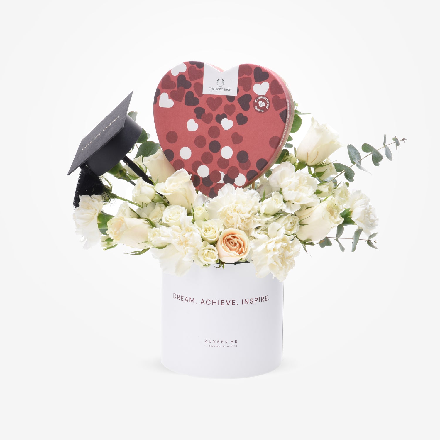 White floral arrangement with graduation cap and heart-shaped chocolate box.