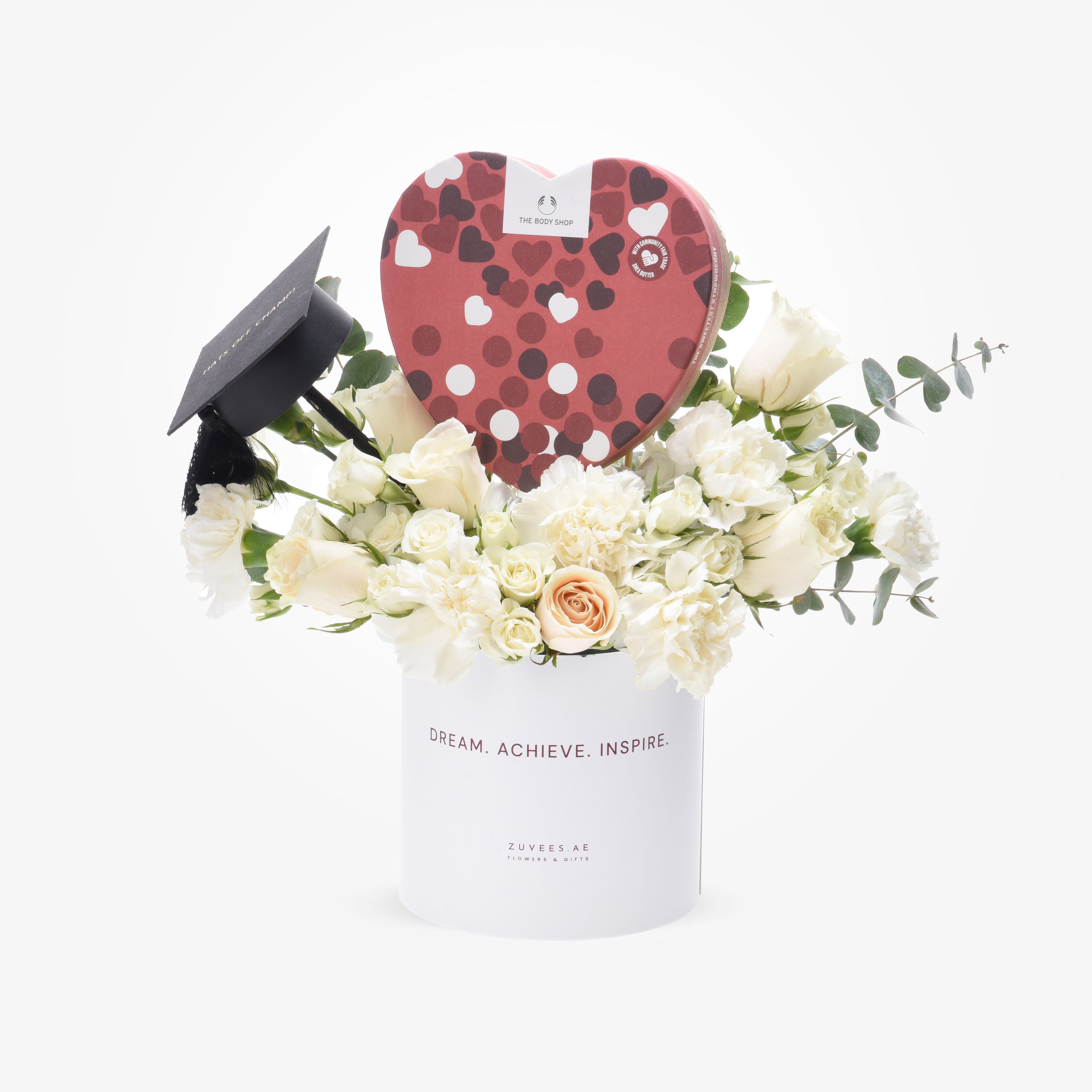 White floral arrangement with graduation cap and heart-shaped chocolate box.
