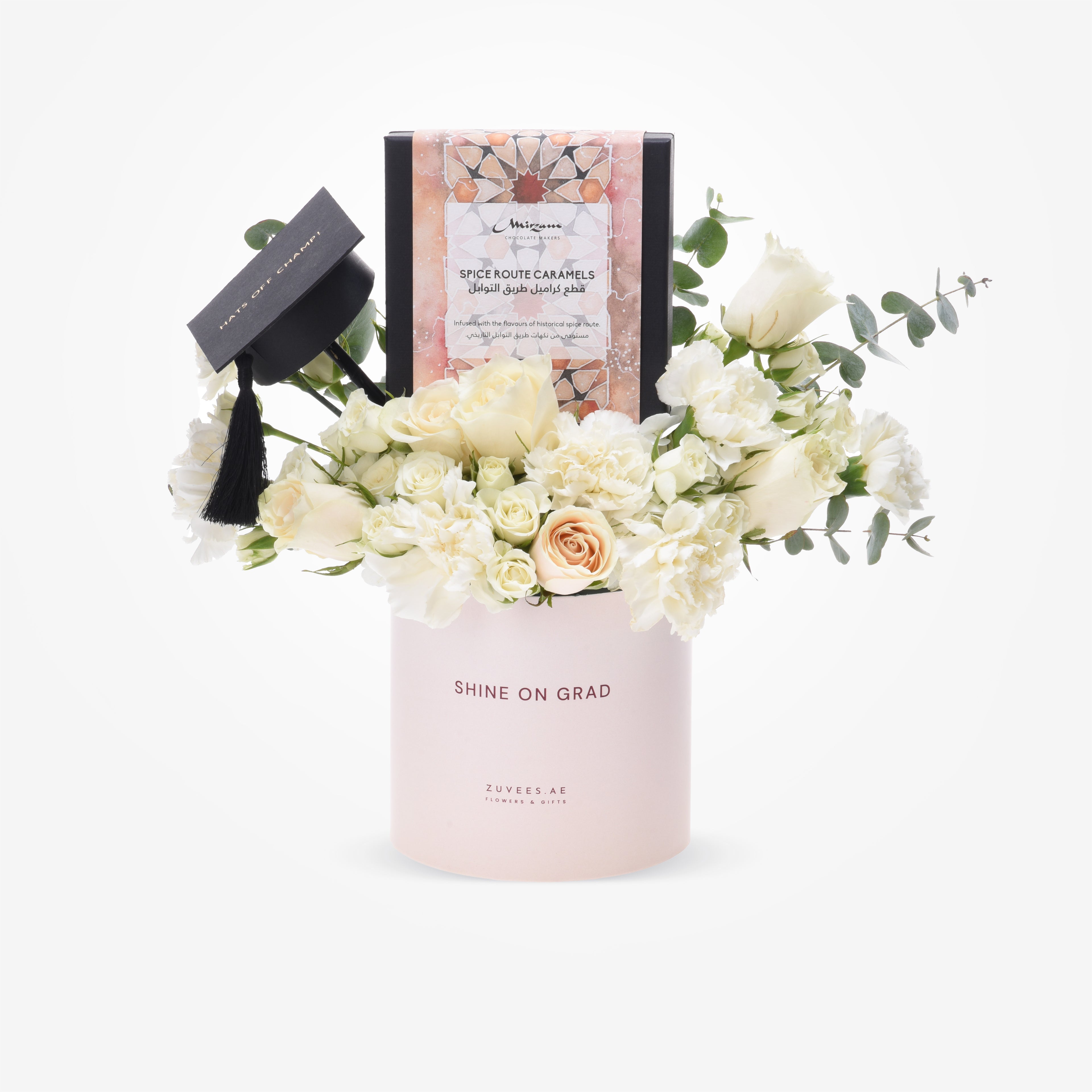 Elegant white roses and eucalyptus in blush pink “Shine On Grad” cylinder with graduation cap and spice caramel gift box.
