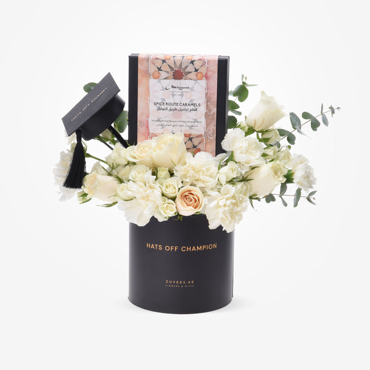 Elegant black graduation-themed floral arrangement with white roses, accented by a mini cap and "Hats Off Champion" text.