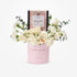 Pink "Congratulations" cylinder holds white roses, eucalyptus, and spice caramel gift box.