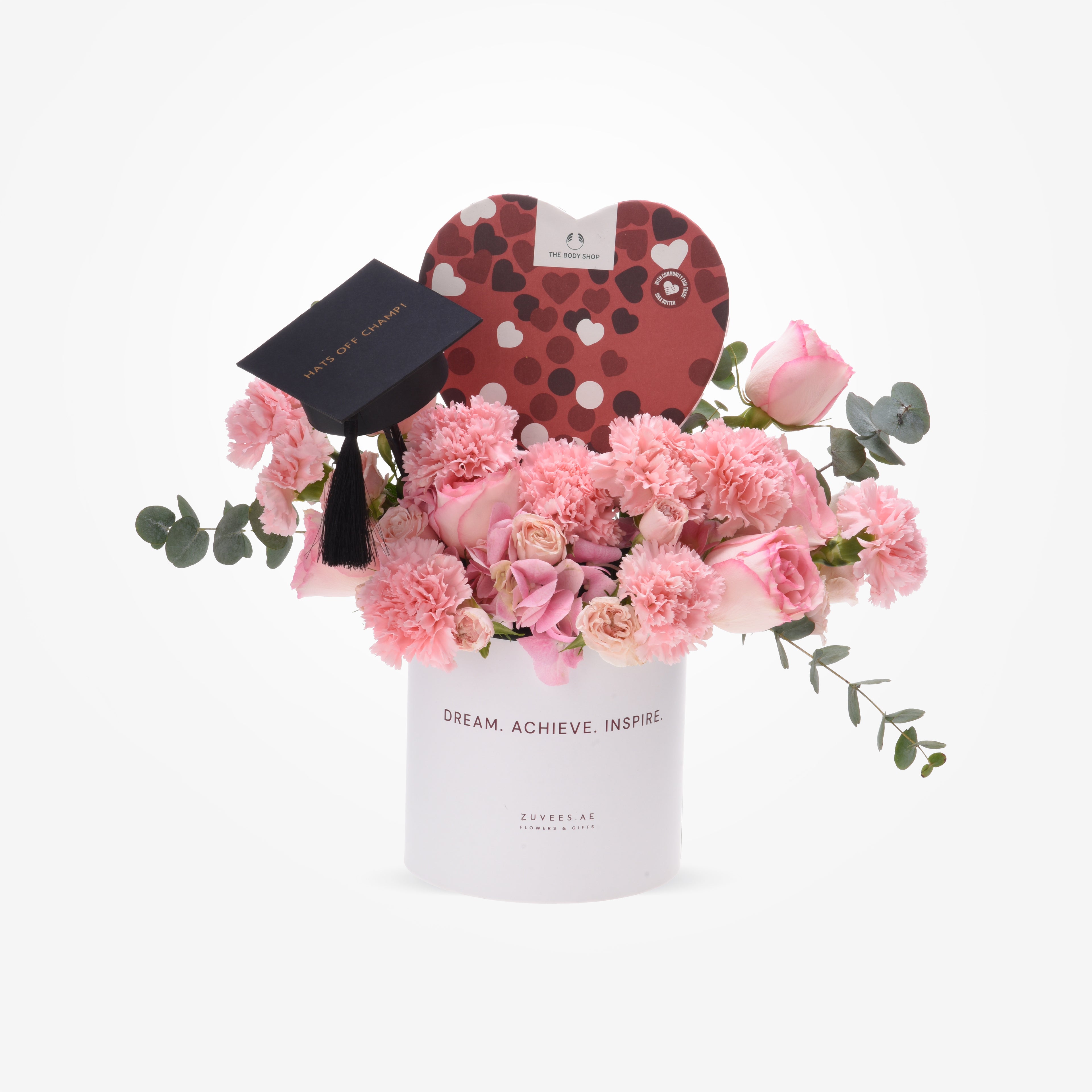 Pink carnations and roses in white vase with graduation cap and heart-shaped gift box.