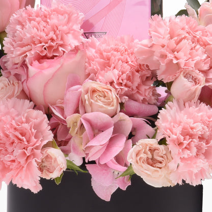 Soft pink carnations and roses in sleek black vase with branded pink box.