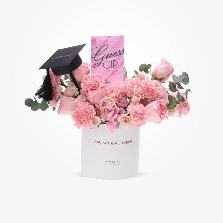 Pink roses and carnations in white cylinder with graduation cap and Guess perfume.