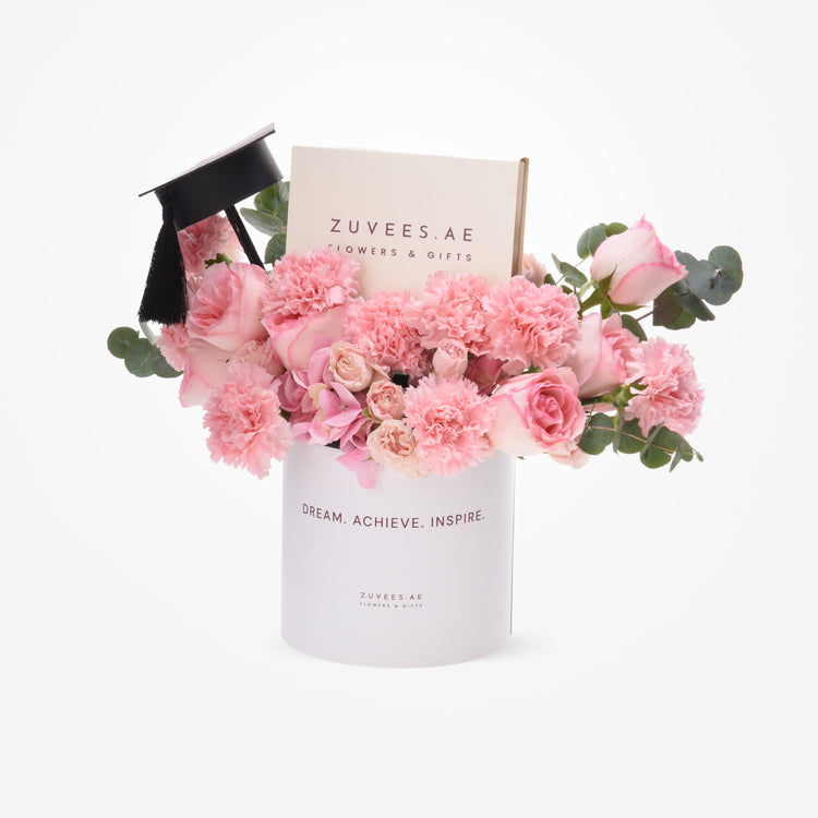 Pink roses and carnations in white cylinder with graduation cap and branded box.