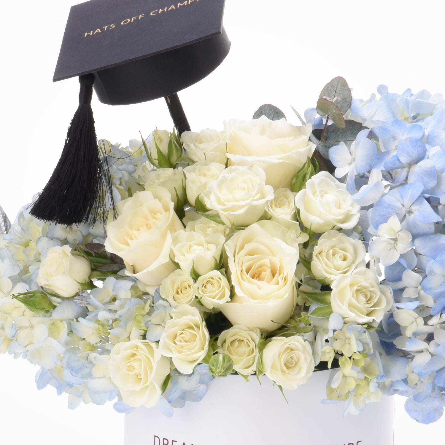 Elegant cream roses and blue hydrangeas crowned with a black graduation cap.