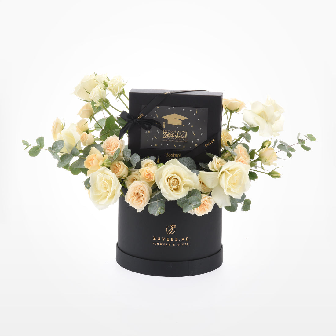 Elegant black box holds creamy roses and eucalyptus, topped with graduation-themed chocolate gift.