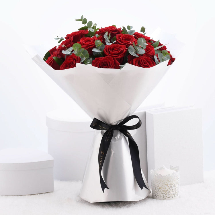 Vibrant red roses wrapped in white paper with black ribbon, elegant gift presentation.