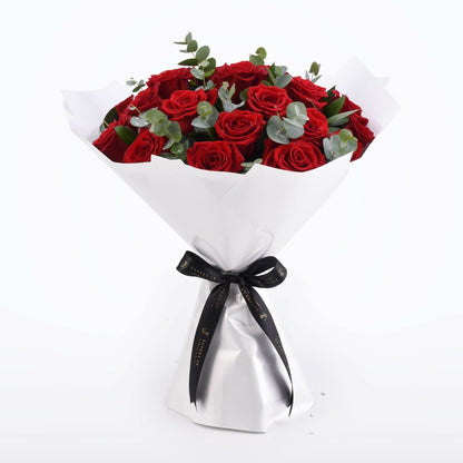 Vibrant red roses with eucalyptus, elegantly wrapped in white paper, tied with black ribbon.
