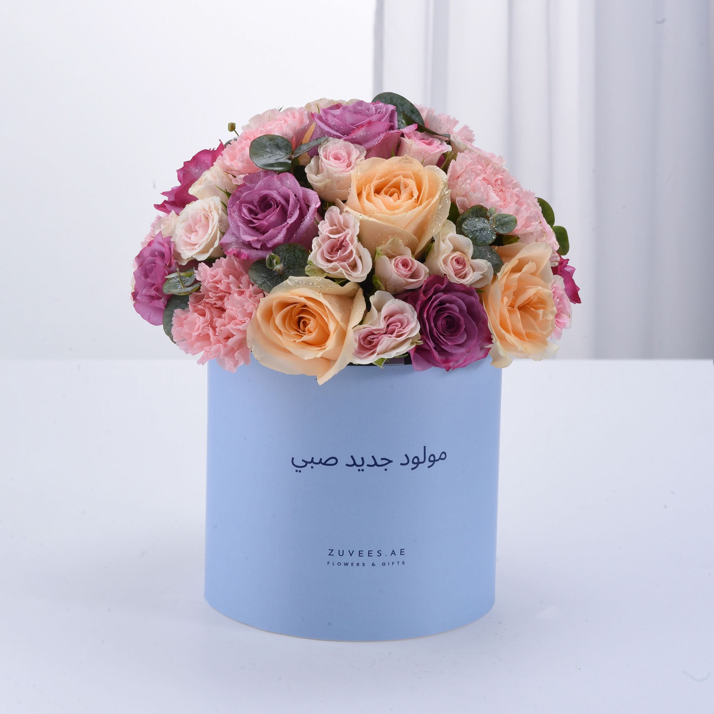 Pastel pink, purple, and peach roses in light blue box with Arabic birthday message.
