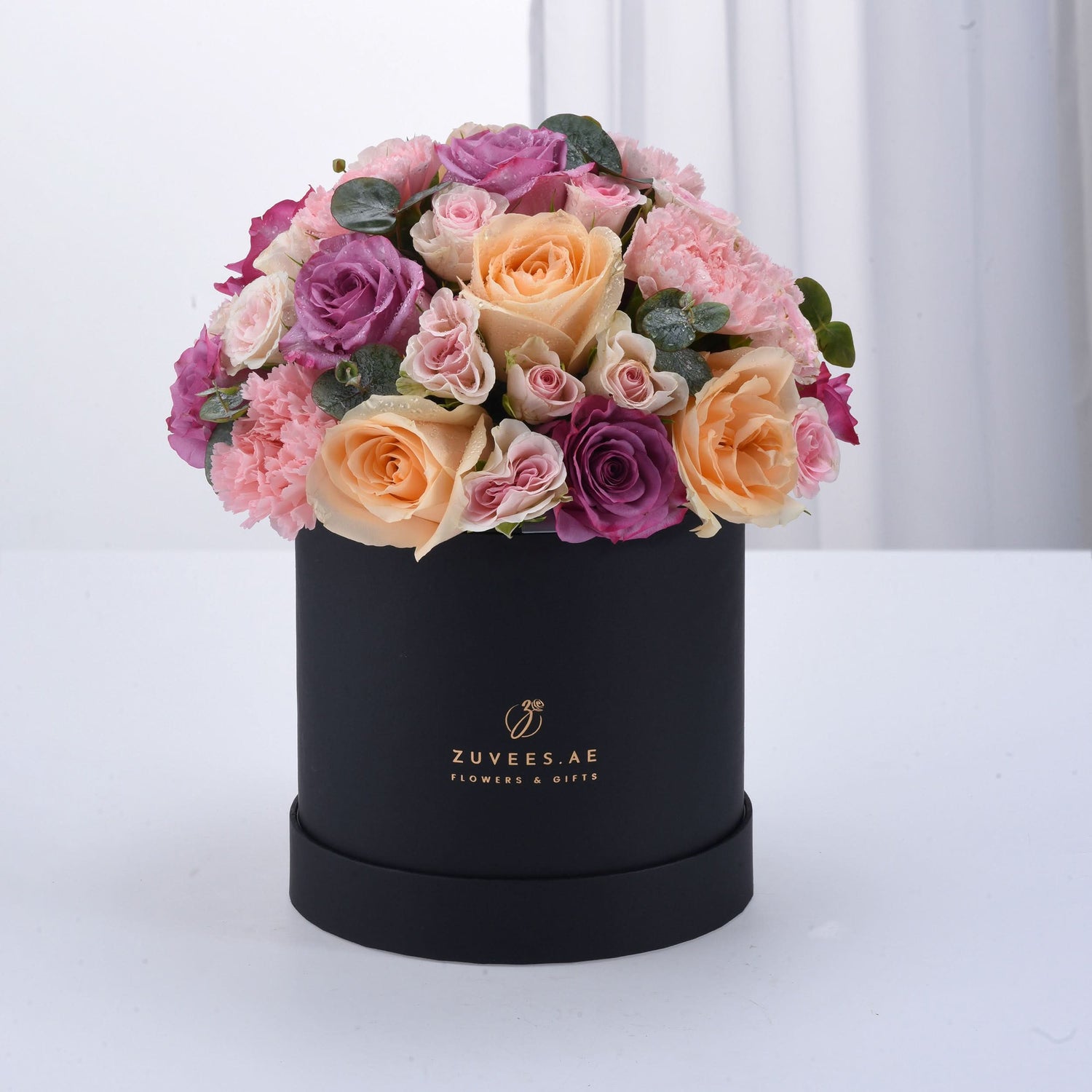 Elegant black box filled with lush pink, peach, and purple roses and carnations.