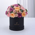 Elegant black box filled with lush pink, peach, and purple roses and carnations.