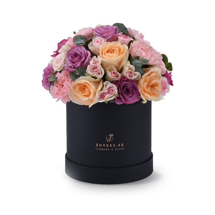 Elegant black hatbox filled with lush pink, purple, and peach roses and carnations.