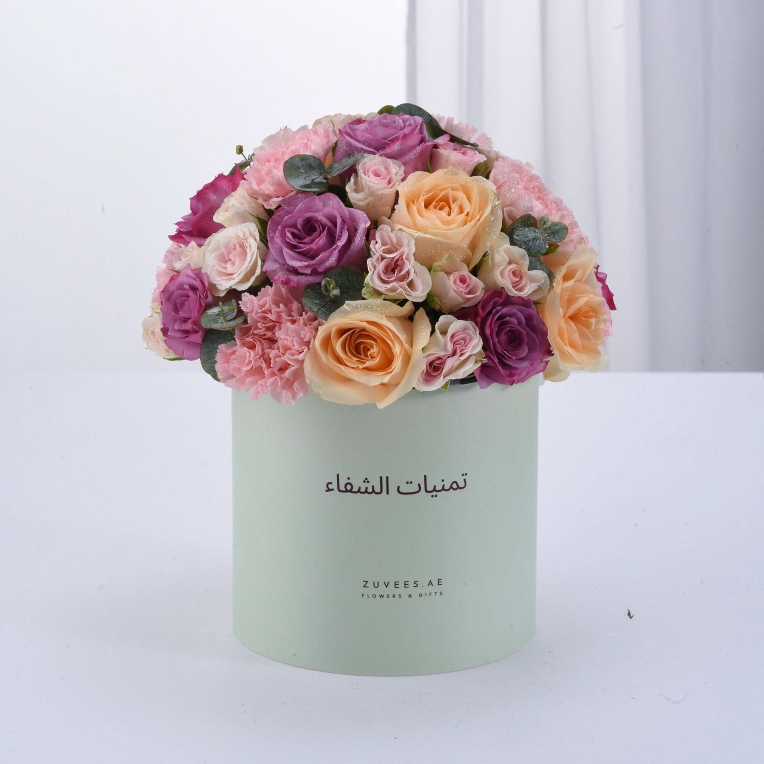 Pastel-hued roses and carnations in mint box with Arabic branding.