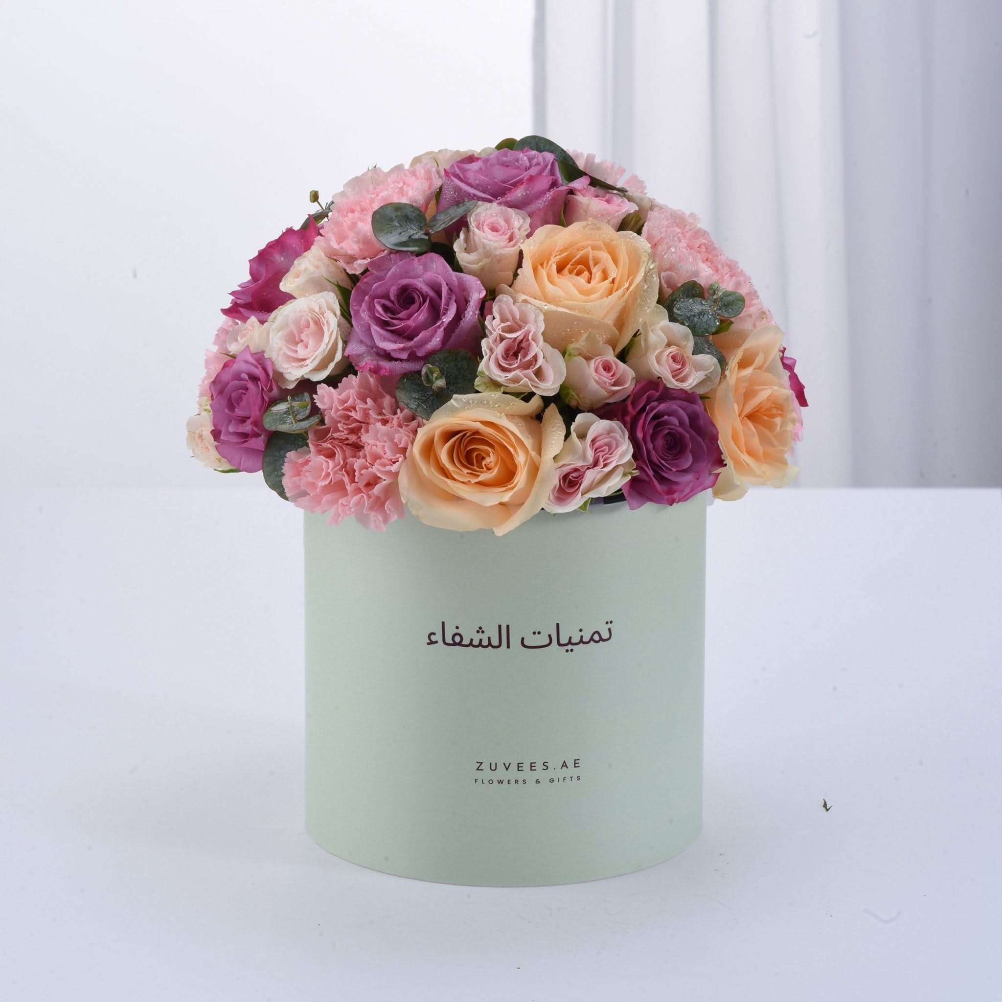 Pastel-hued roses and carnations in mint box with Arabic branding.