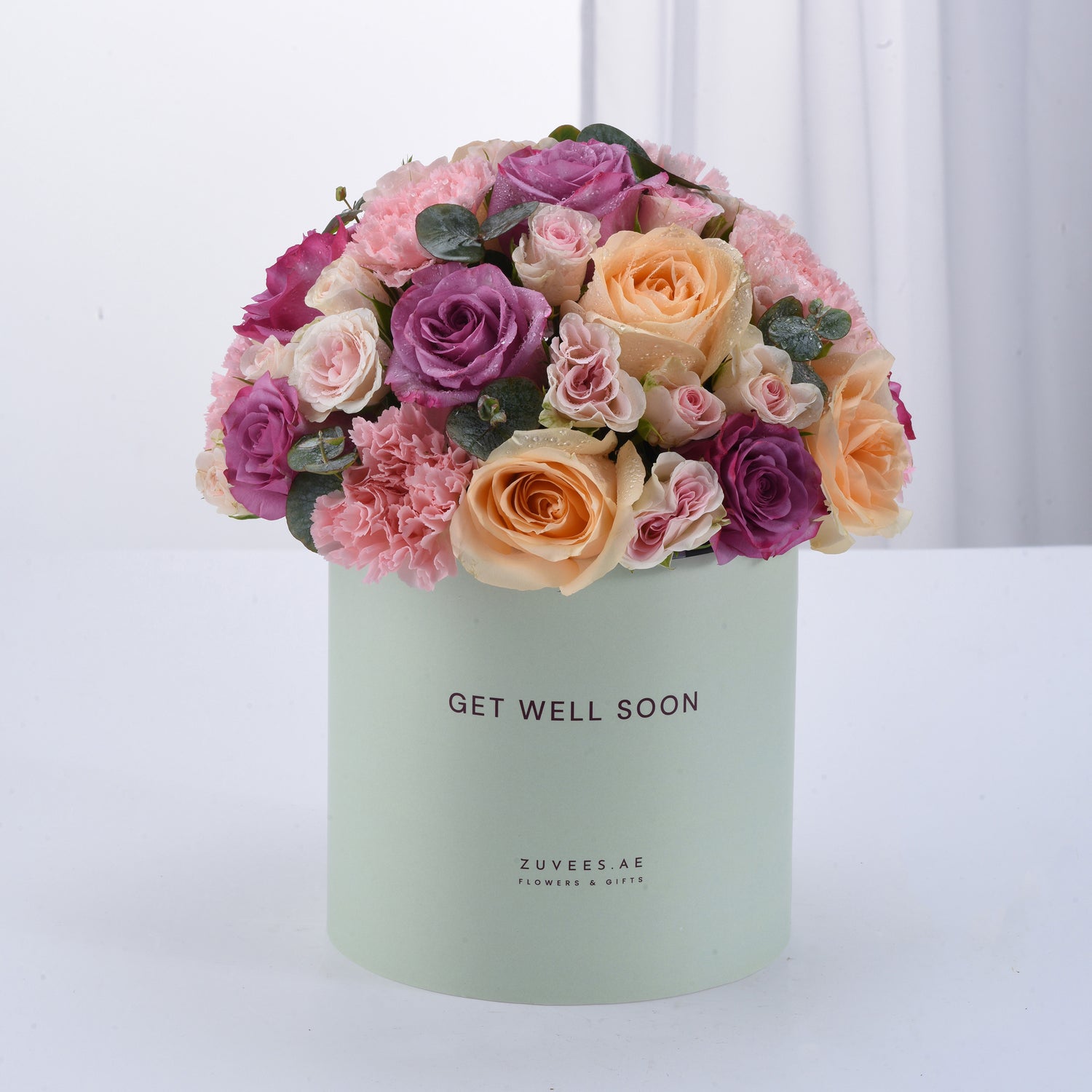 Pastel green box holds vibrant pink, purple, and peach roses with "Get Well Soon" message.